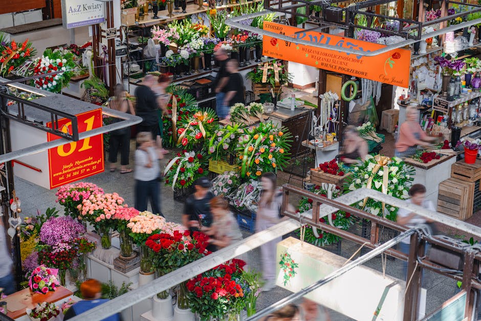 Indoor flower market scene showcasing vibrant floral arrangements and bouquets with a variety of flowers including pink, red, purple, and white blossoms. Flower arrangements are displayed in vases, ba